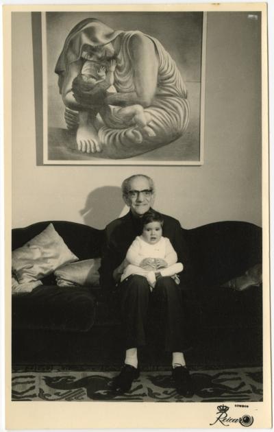 Almada with his first granddaughter, Rita, on his lap, underneath his painting Maternidade (Maternity) (1935).